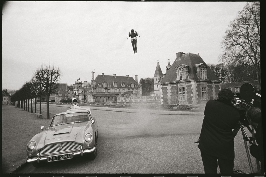 The force of the jet pack can be seen whipping up the dust and stones on the road as it comes into land.Waiting at the Aston Martin DB5 is French spy Madame LaPorte. played by MARYSE GUY MITSOUKO. 