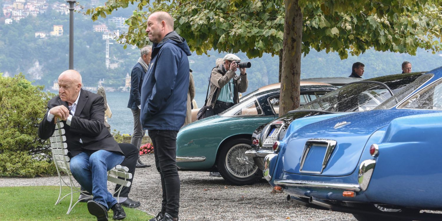 Man sitting on bench at Villa d'Este near the shore of Lake Como in Italy with parked cars nearby