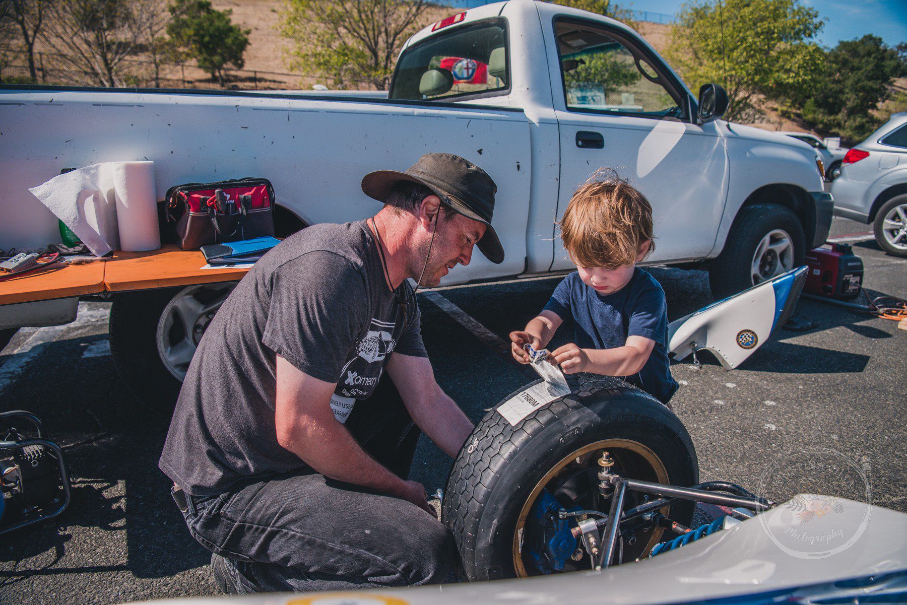 A young race enthusiast helps his Dad prep the race car in the Paddock