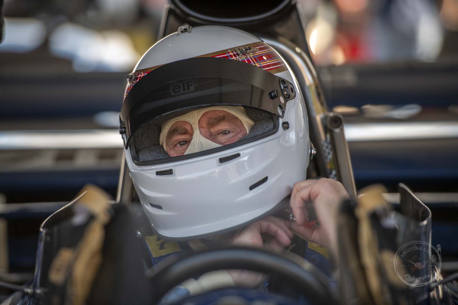 A racecar driver fastens the chin strap on his helmet 
