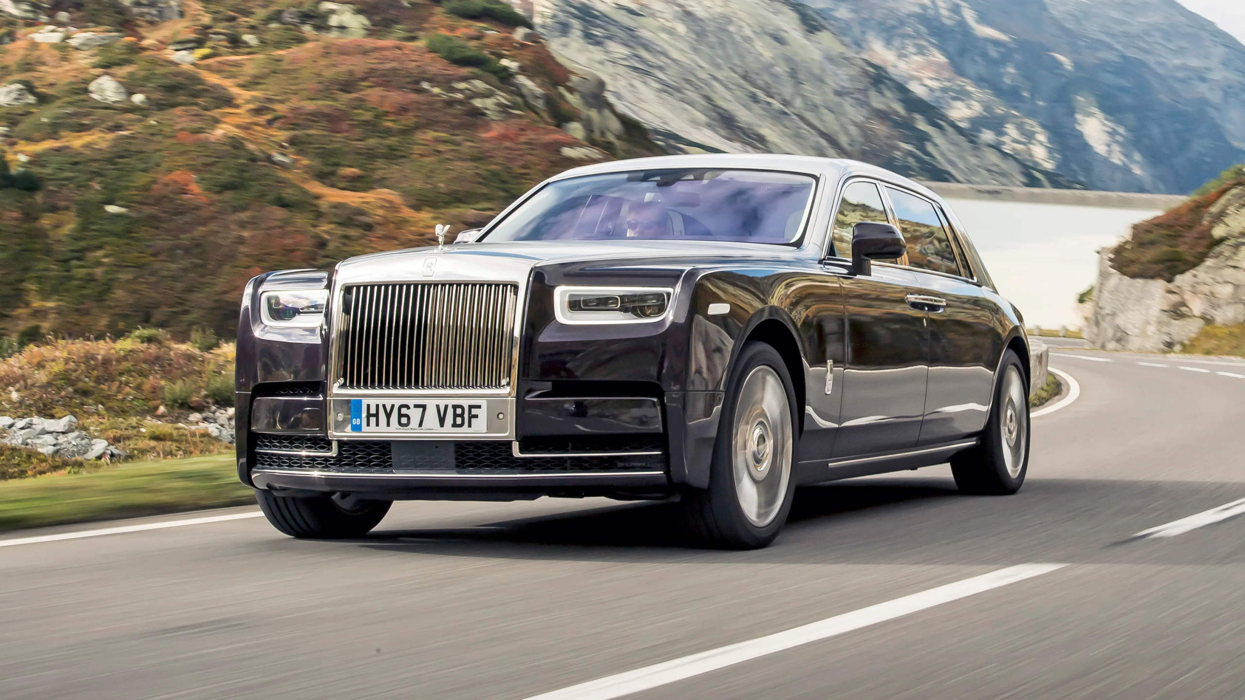 Three-quarter front view of a 2026 Rolls-Royce Phantom driving on a scenic mountain road