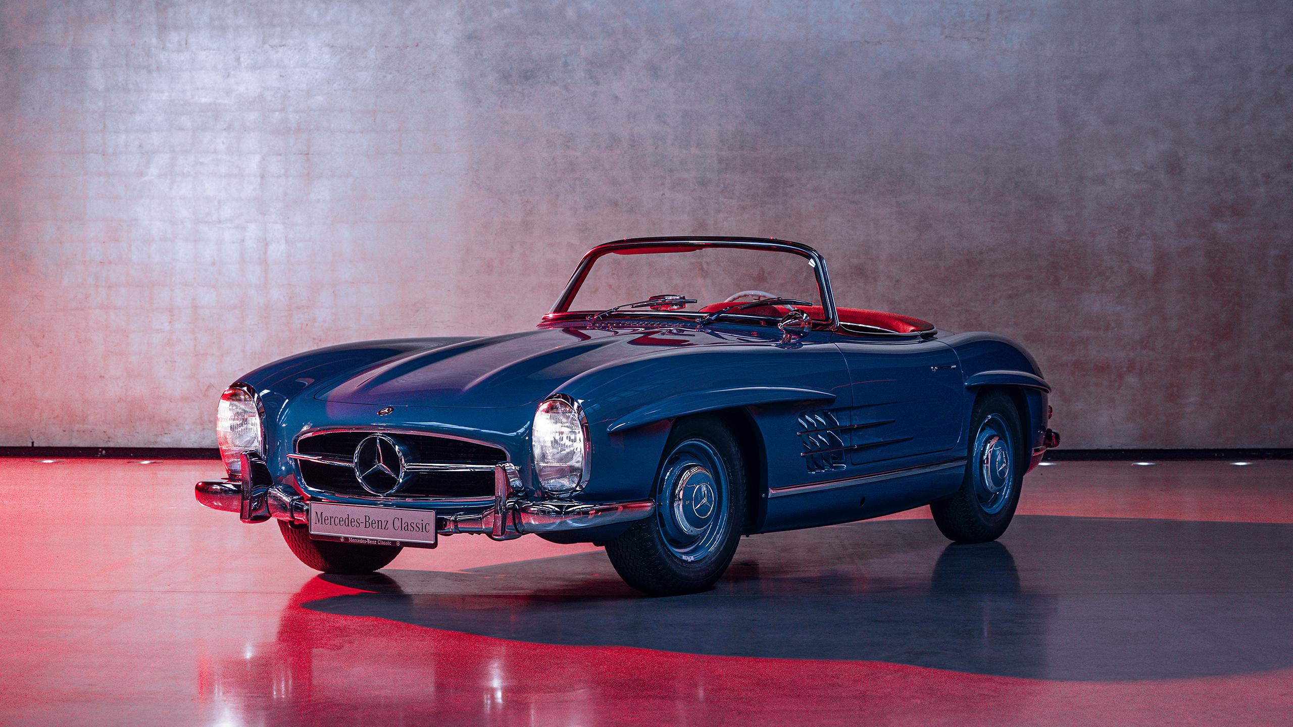 A classic blue Mercedes-Benz 300 SL Roadster with a red interior, parked in a studio with dramatic lighting.
