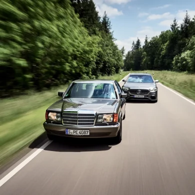 Classic Mercedes-Benz S-Class driving alongside a modern Mercedes-AMG S-Class on a forest road.