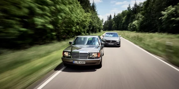 Classic Mercedes-Benz S-Class driving alongside a modern Mercedes-AMG S-Class on a forest road.