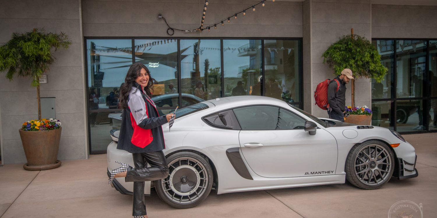 Salena from Porsche Monterey waves the checkered flag while showing off her race attire in front of a Porsche GT4 RS.