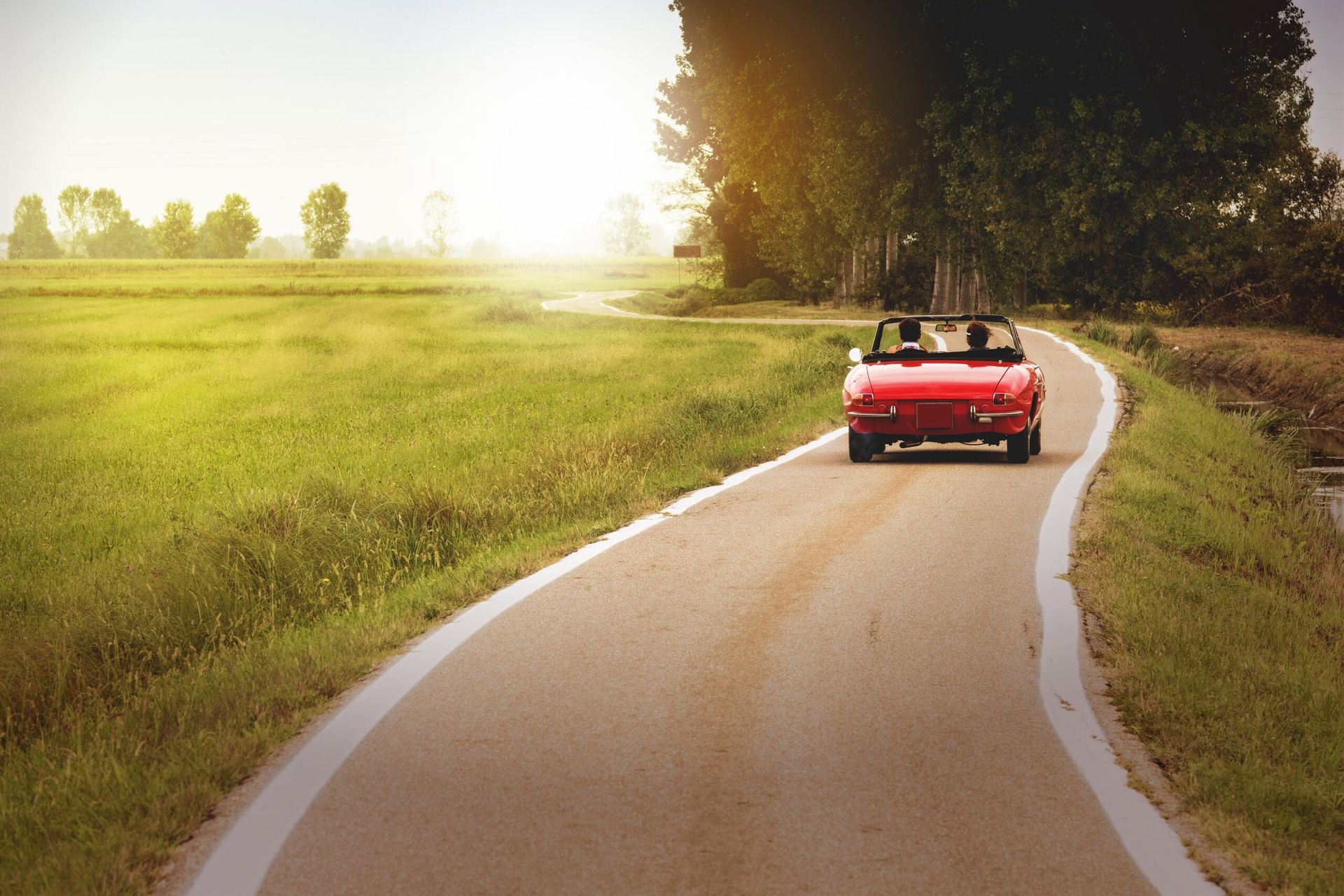 Red classic convertible car driving in the countryside